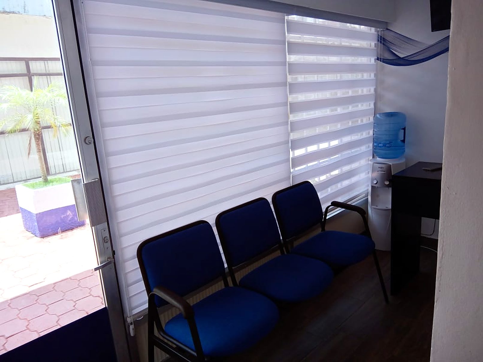 Sala de espera de FISIOAR con sillas azules, persianas claras y dispensador de agua